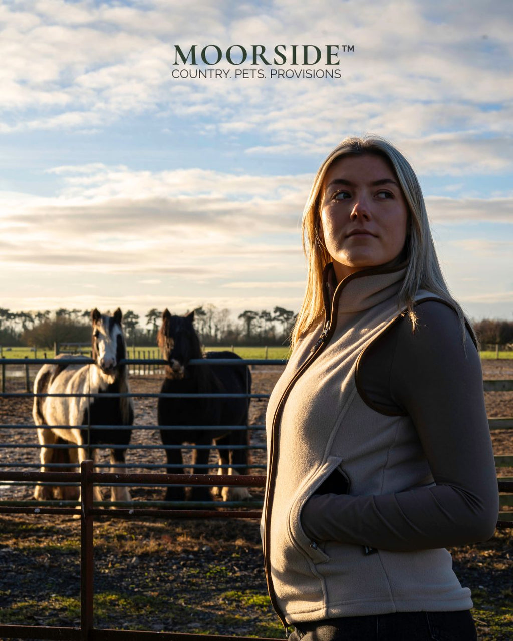 Woman standing in a field with horses, featuring the Moorside brand.